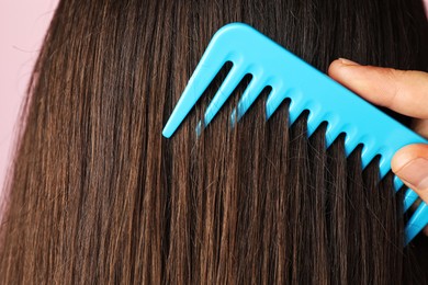 Photo of Woman brushing hair with plastic comb on pink background, closeup