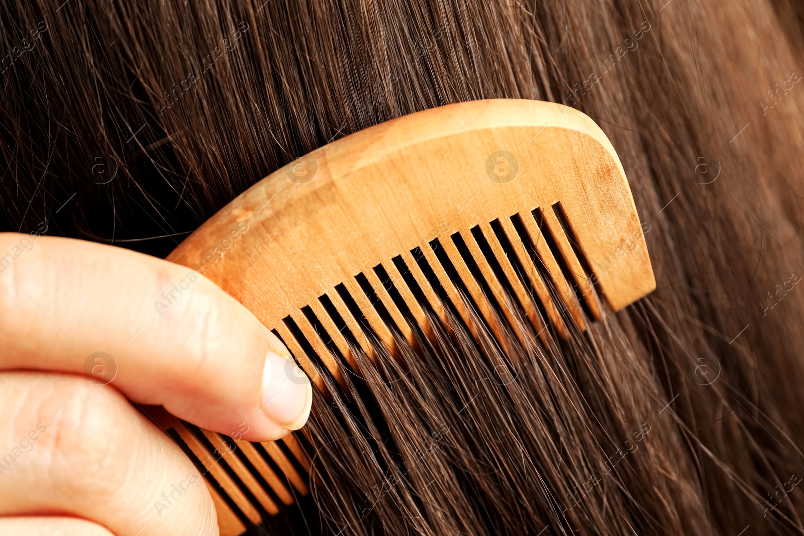 Photo of Woman brushing hair with wooden comb, closeup