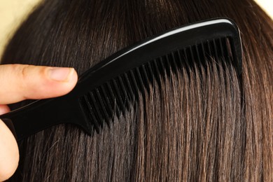 Photo of Woman brushing hair with plastic comb, closeup