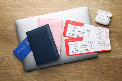 Photo of Travel agency. Flight tickets, passports, credit card, earphones and laptop on wooden table, flat lay