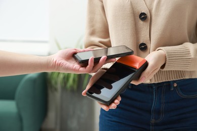 Photo of Woman paying for service with smartphone via terminal indoors, closeup