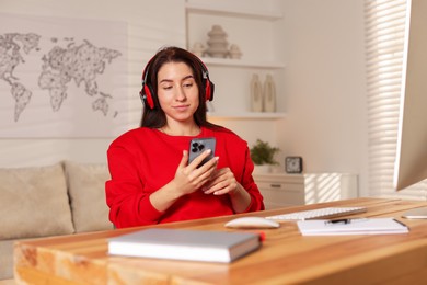 Photo of Woman with smartphone and headphones working at desk in home office