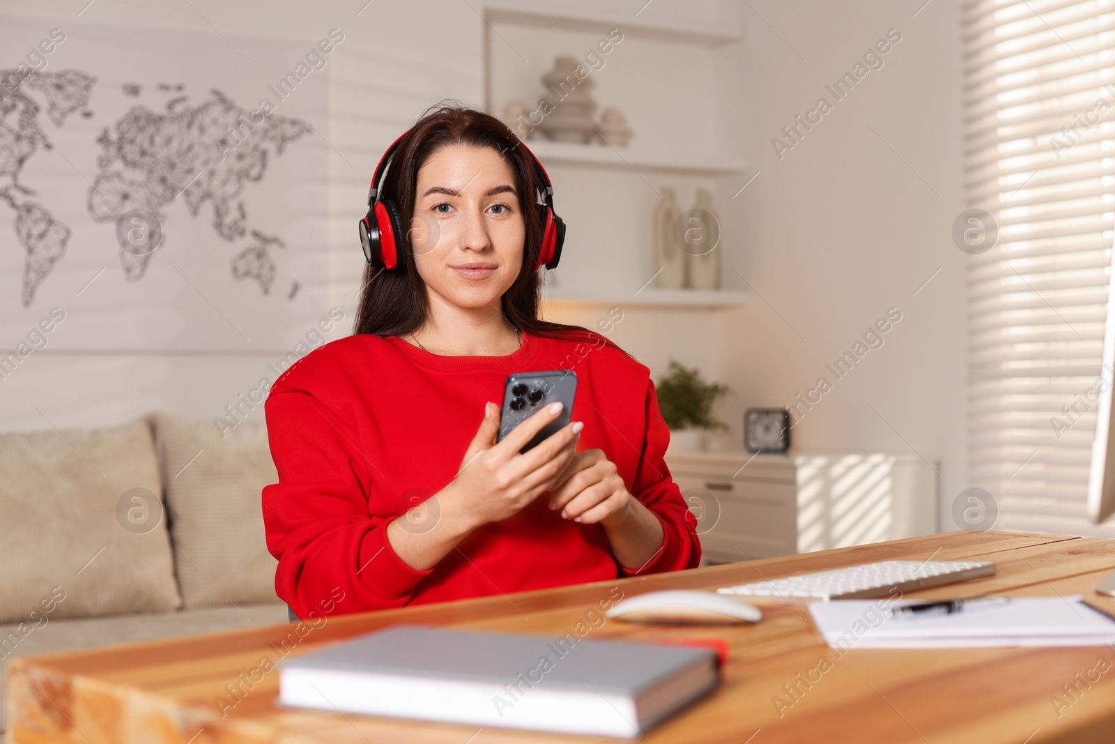 Photo of Woman with smartphone and headphones working at desk in home office