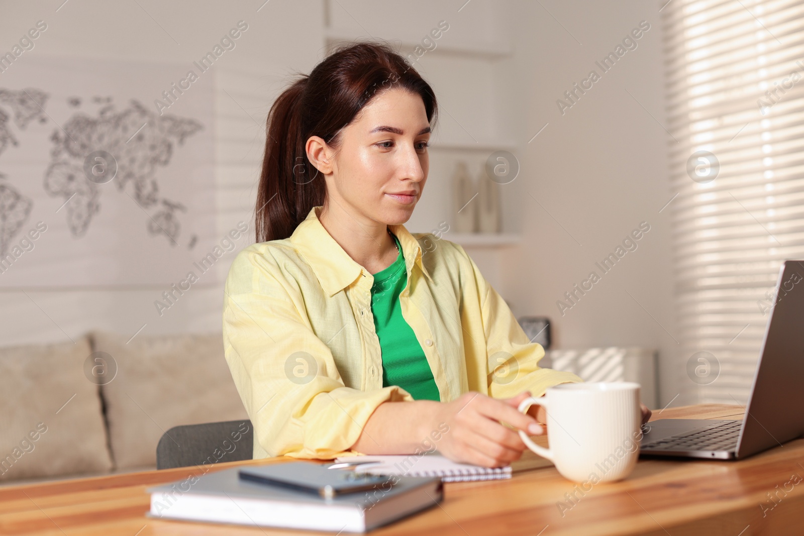 Photo of Young woman working on laptop at desk in home office