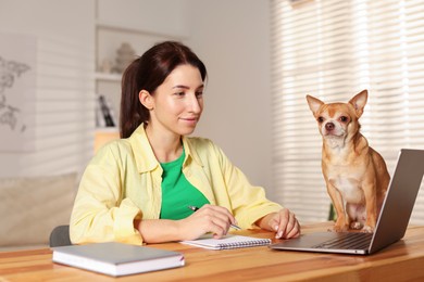 Photo of Young woman with her cute dog working on laptop at desk in home office