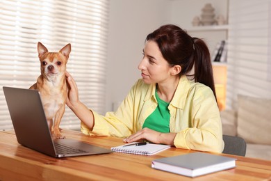 Photo of Young woman with her cute dog working on laptop at desk in home office