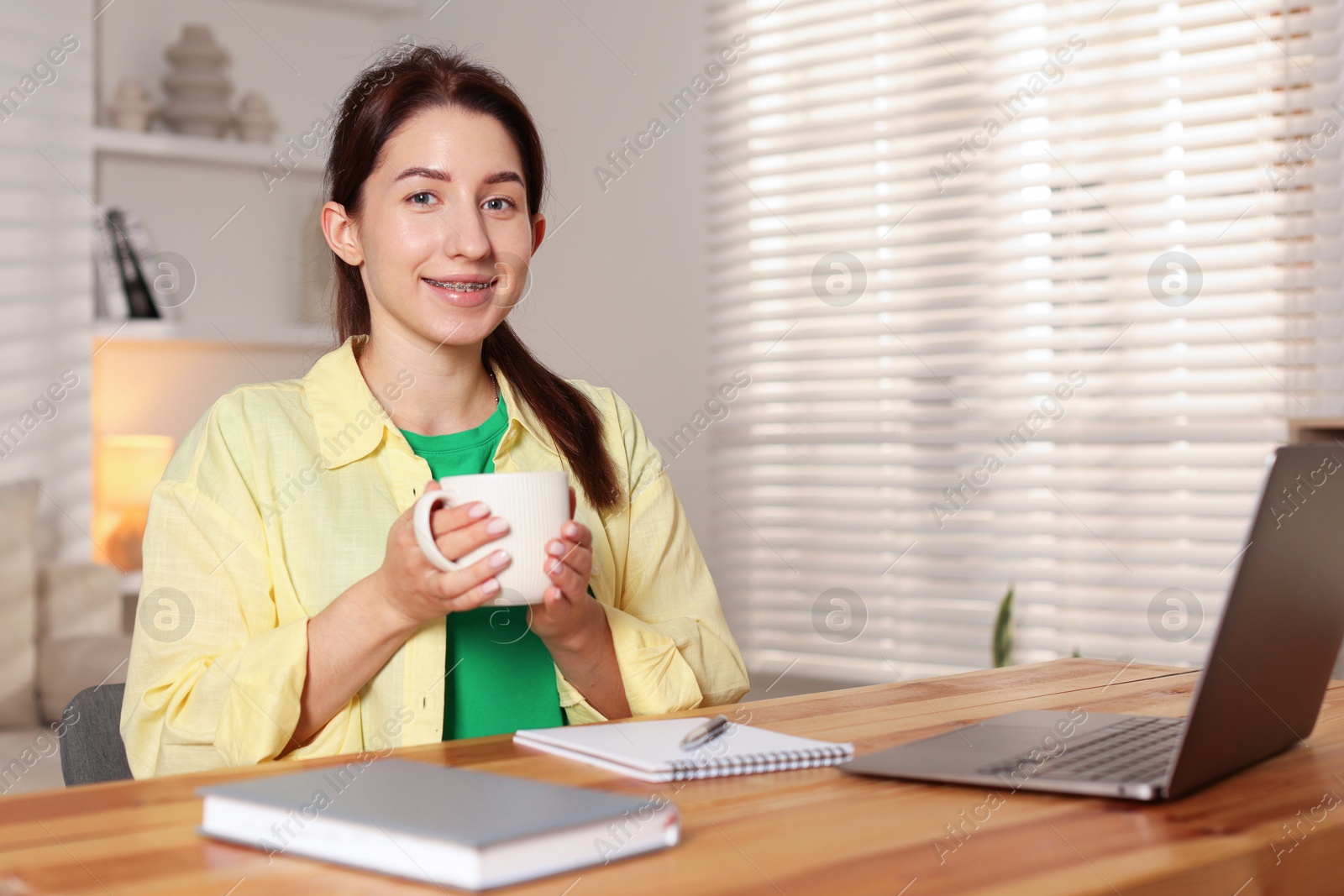 Photo of Young woman with cup of coffee working on laptop at desk in home office. Space for text