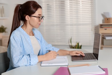 Photo of Young woman working on laptop at desk in home office. Space for text