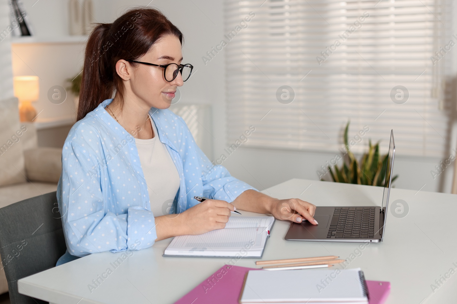 Photo of Young woman working on laptop at desk in home office. Space for text