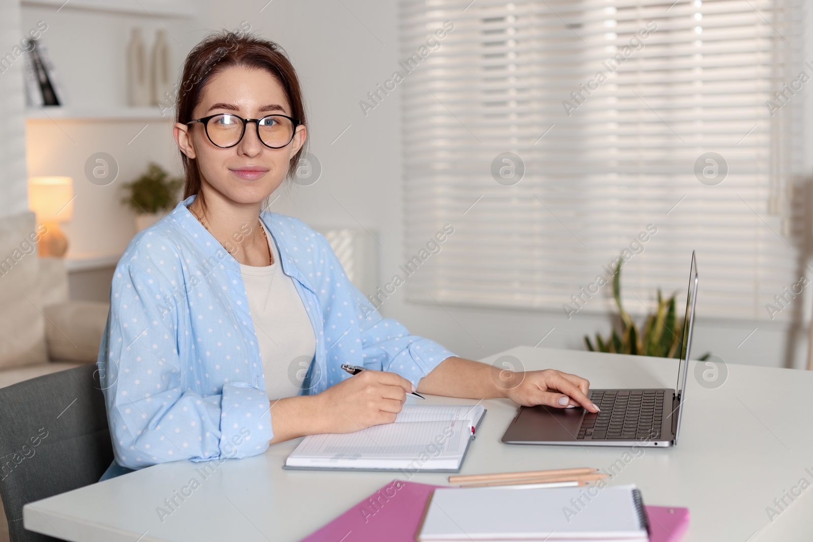 Photo of Young woman working on laptop at desk in home office. Space for text