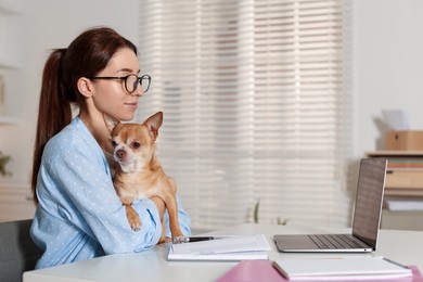 Photo of Young woman with her cute dog working on laptop at desk in home office. Space for text