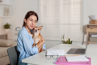 Photo of Young woman with her cute dog working on laptop at desk in home office. Space for text