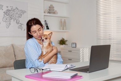 Photo of Young woman with her cute dog working on laptop at desk in home office. Space for text