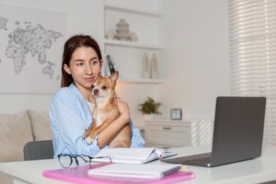 Photo of Young woman with her cute dog working on laptop at desk in home office. Space for text