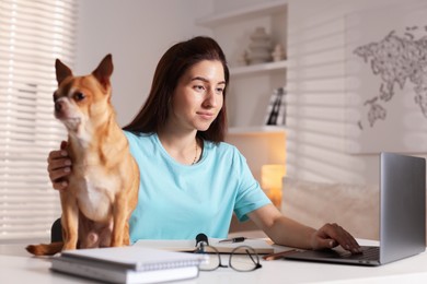 Photo of Young woman with her cute dog working on laptop at desk in home office, selective focus