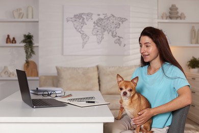 Photo of Young woman with her cute dog working on laptop at desk in home office. Space for text