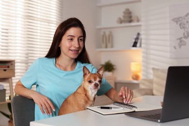 Photo of Young woman with her cute dog working on laptop at desk in home office