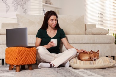 Photo of Young woman working on laptop while her cute dog sleeping beside at home