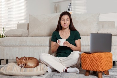 Photo of Young woman working on laptop while her cute dog sleeping beside at home