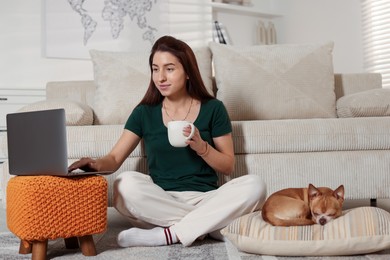 Photo of Young woman working on laptop while her cute dog sleeping beside at home