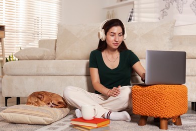 Photo of Young woman working on laptop while her cute dog sleeping beside at home