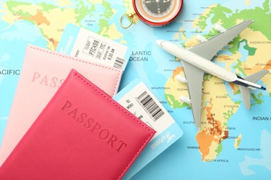 Photo of Passports with tickets, compass and plane model on world map, flat lay