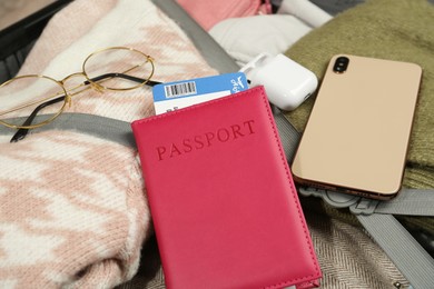 Photo of Passport with ticket, smartphone, earphones and glasses on packed suitcase, closeup