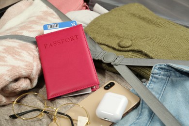 Photo of Passport with ticket, smartphone, earphones and glasses on packed suitcase, closeup