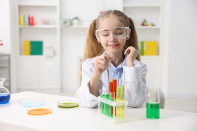 Photo of Little girl doing chemical experiment at desk indoors