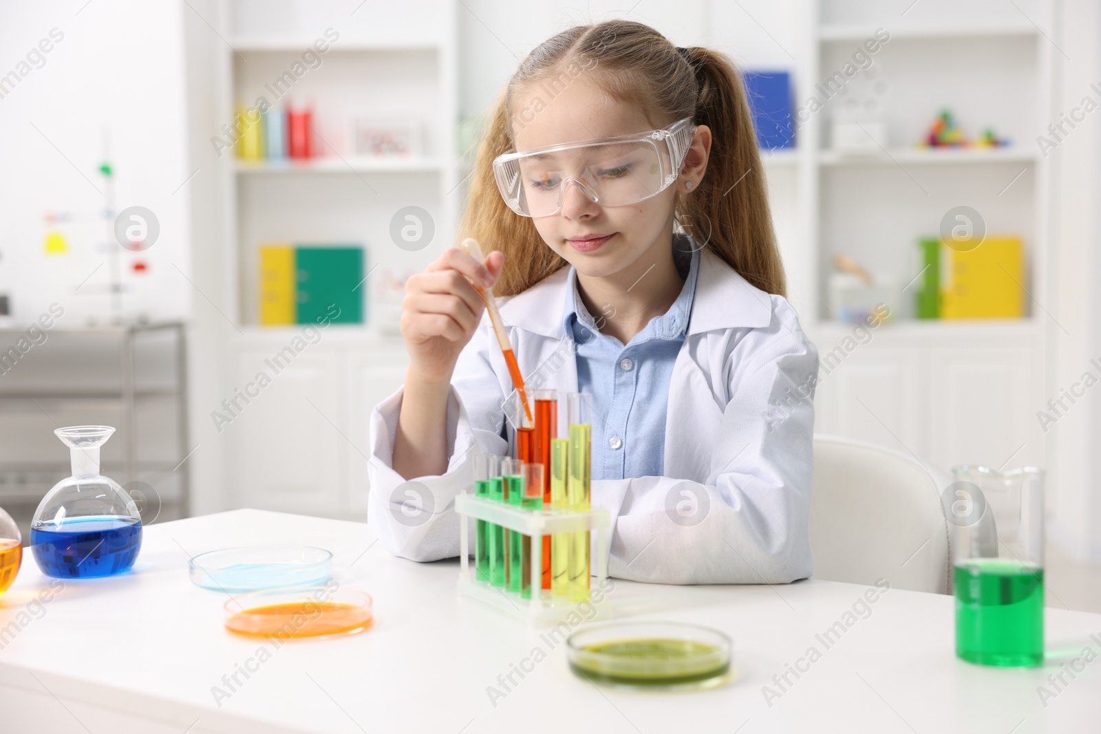 Photo of Little girl doing chemical experiment at desk indoors