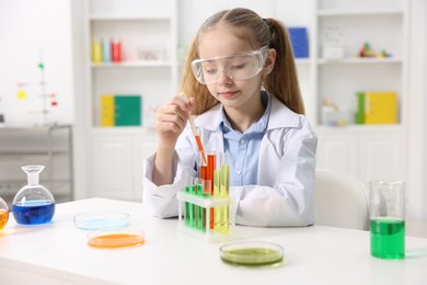 Photo of Little girl doing chemical experiment at desk indoors