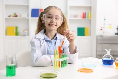 Photo of Little girl doing chemical experiment at desk indoors