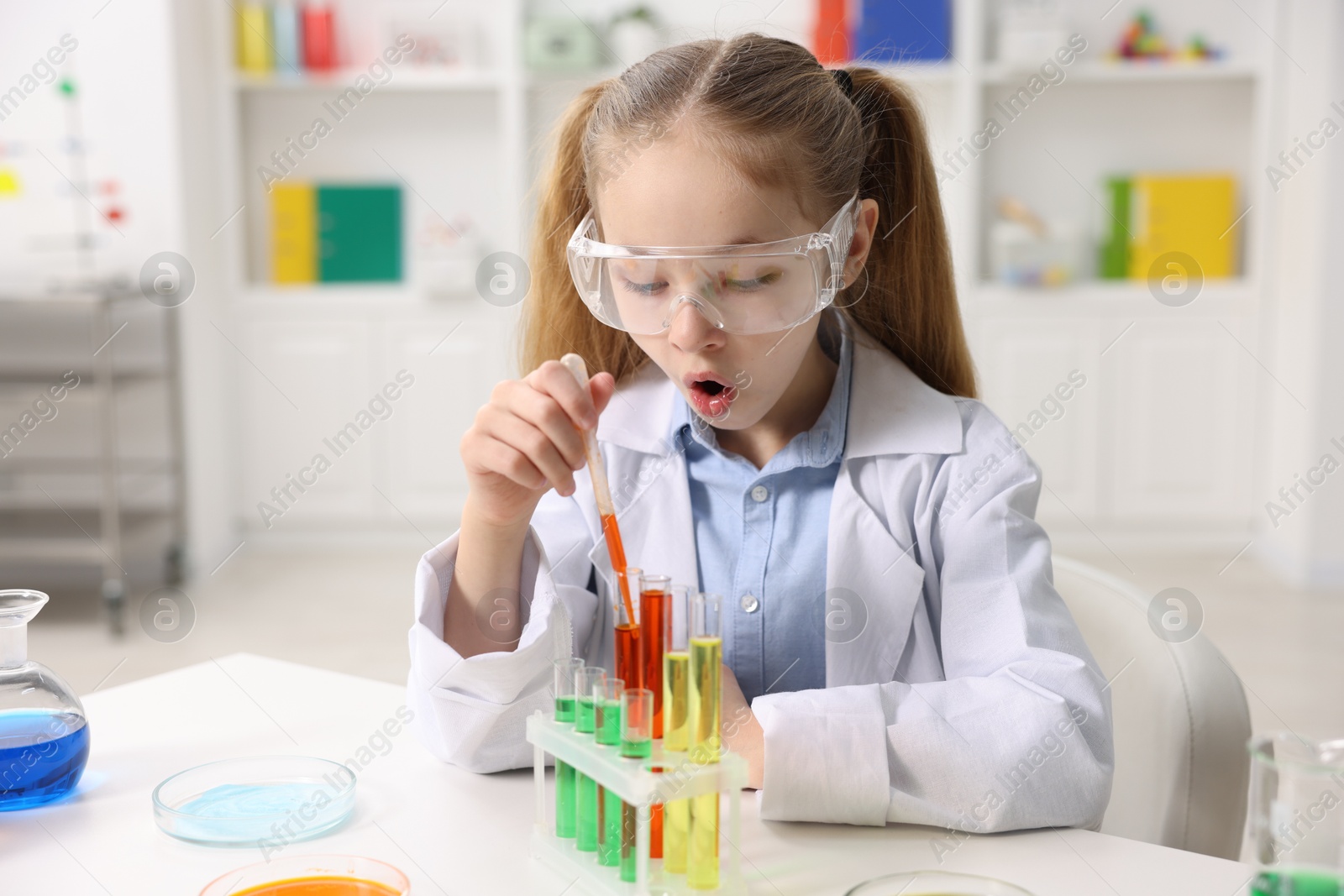 Photo of Little girl doing chemical experiment at desk indoors