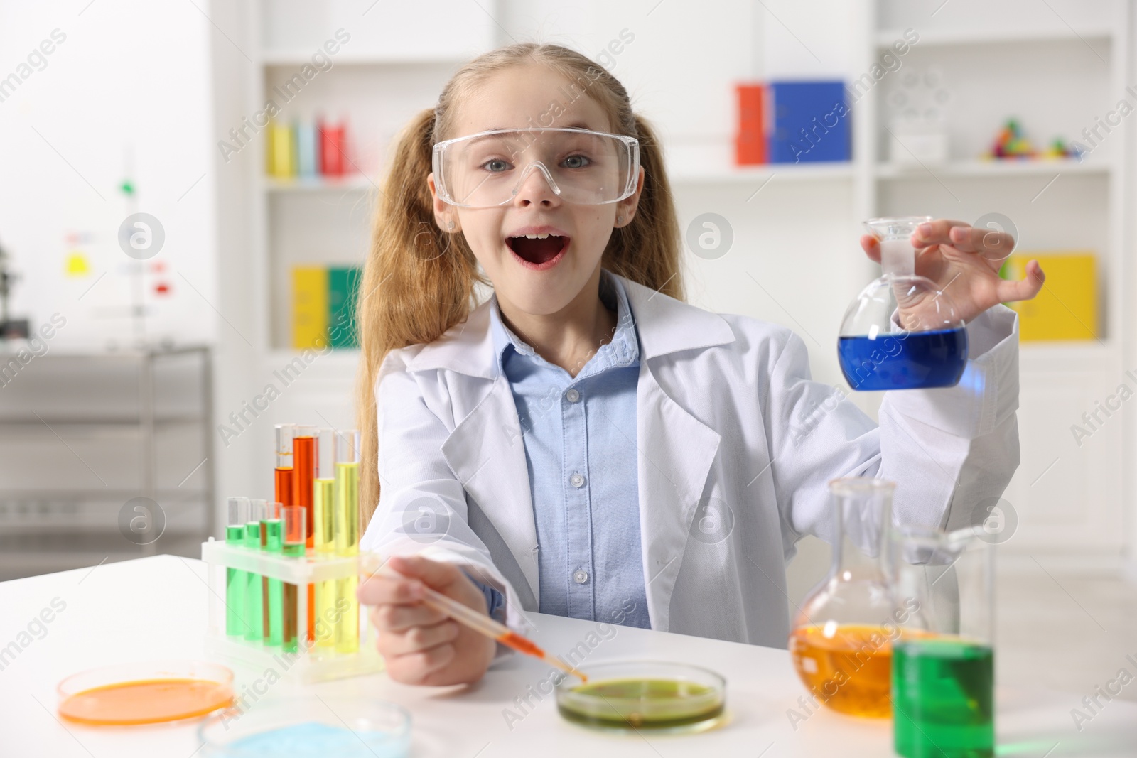 Photo of Little girl doing chemical experiment at desk indoors