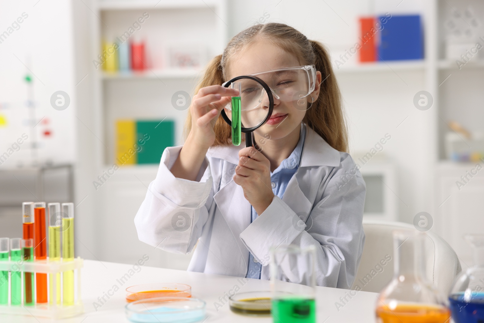 Photo of Little girl doing chemical experiment at desk indoors