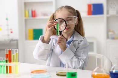 Photo of Little girl doing chemical experiment at desk indoors