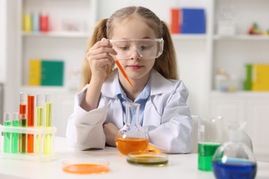 Photo of Little girl doing chemical experiment at desk indoors