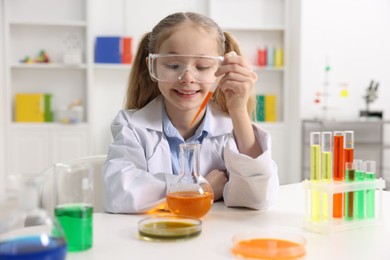 Photo of Little girl doing chemical experiment at desk indoors