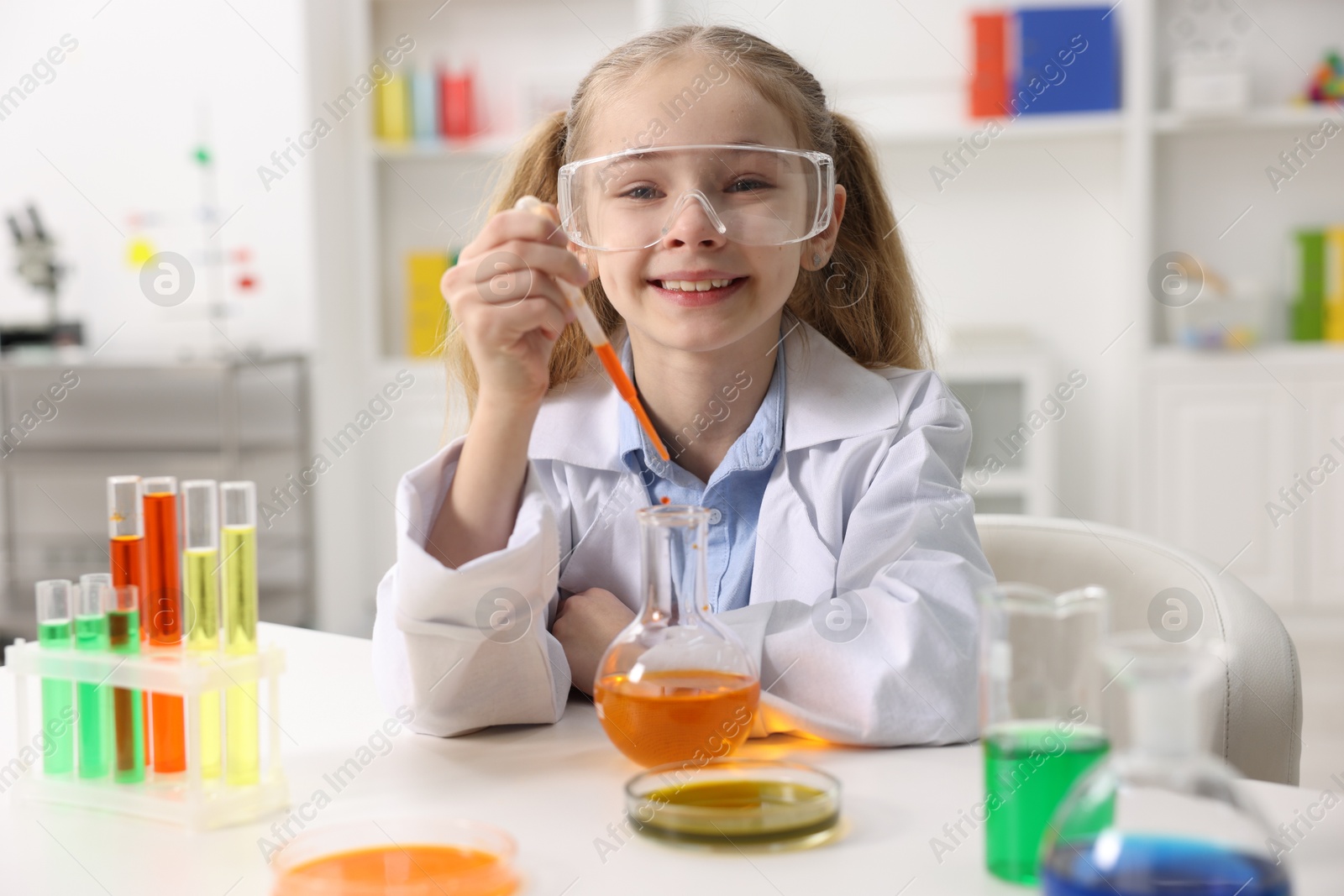 Photo of Little girl doing chemical experiment at desk indoors