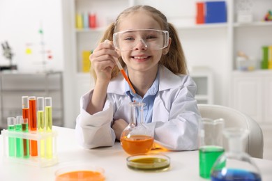 Photo of Little girl doing chemical experiment at desk indoors