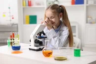 Photo of Little girl working with microscope at desk indoors