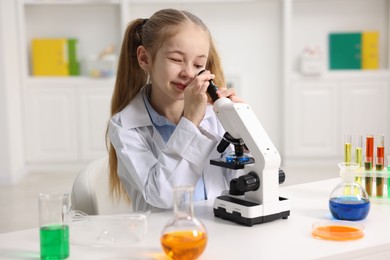 Photo of Little girl working with microscope at desk indoors