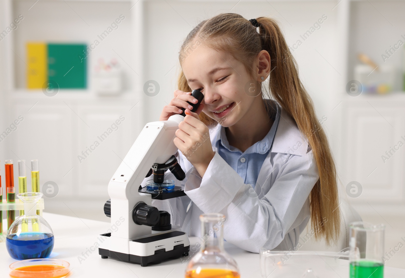 Photo of Little girl working with microscope at desk indoors