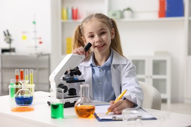 Photo of Little girl working with microscope at desk indoors