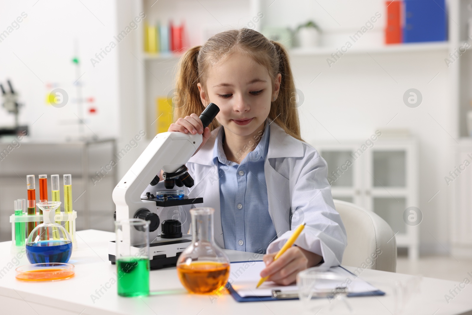 Photo of Little girl working with microscope at desk indoors