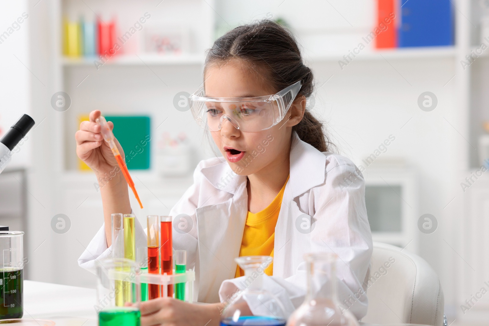 Photo of Little girl doing chemical experiment at desk indoors