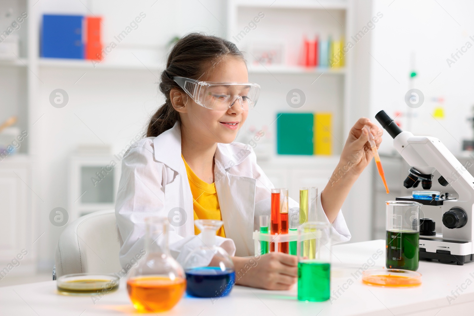 Photo of Little girl doing chemical experiment at desk indoors