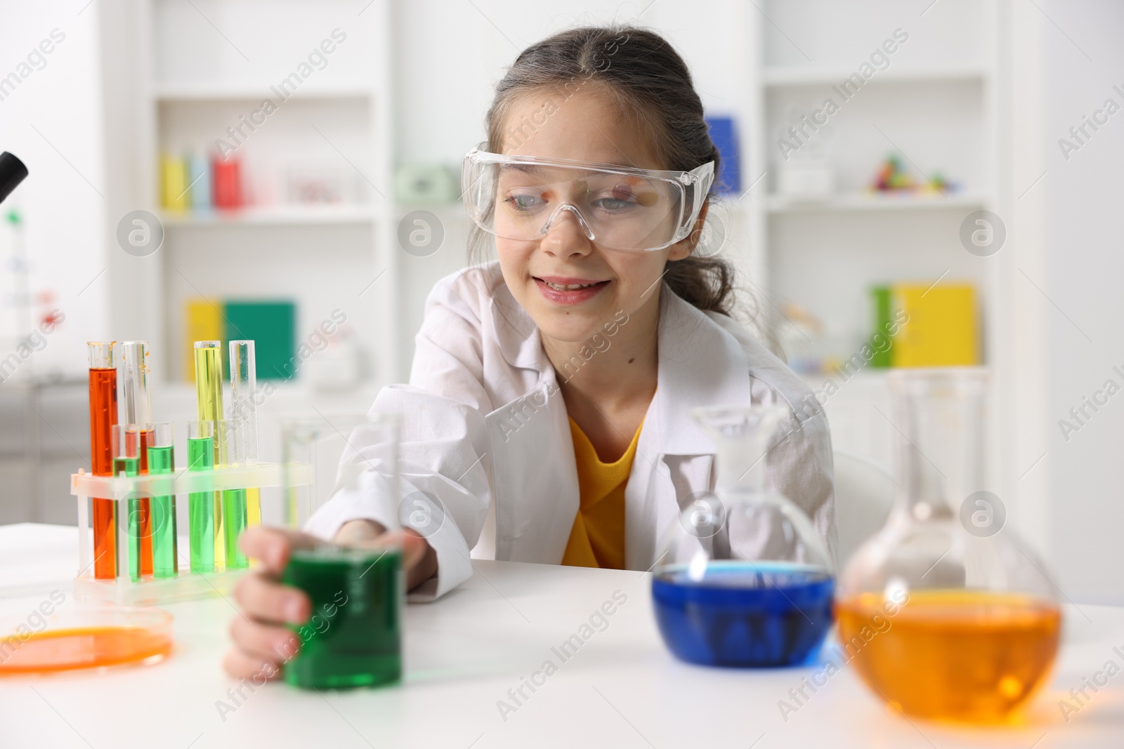 Photo of Little girl doing chemical experiment at desk indoors