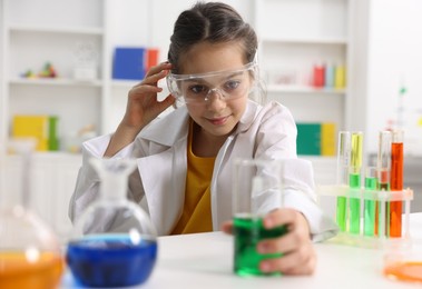 Photo of Little girl doing chemical experiment at desk indoors