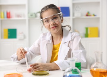 Photo of Little girl doing chemical experiment at desk indoors